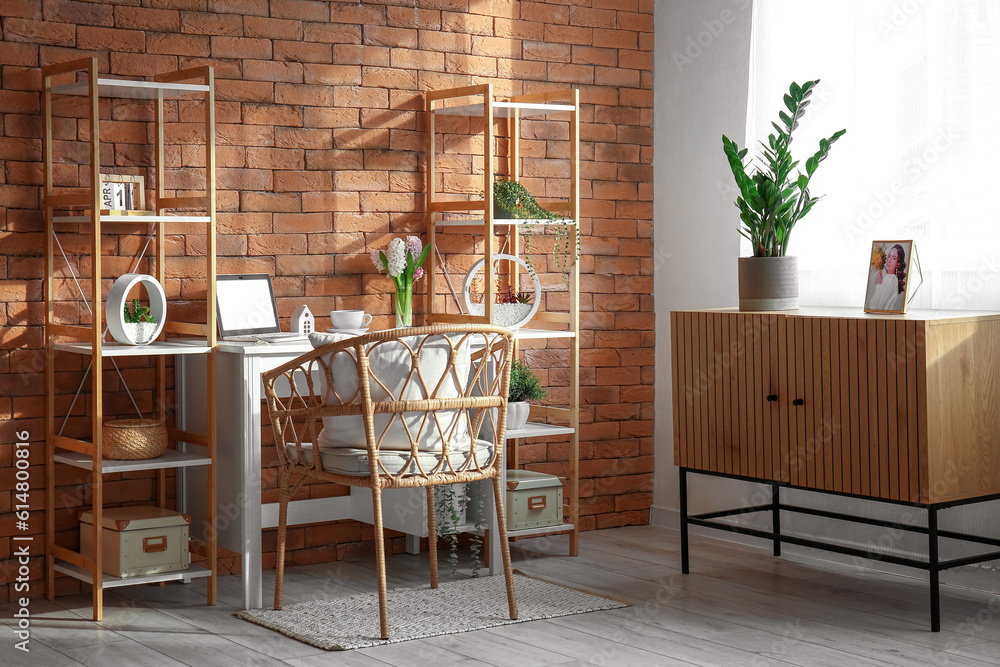 Comfortable workplace with modern laptop and hyacinth flowers near brown brick wall