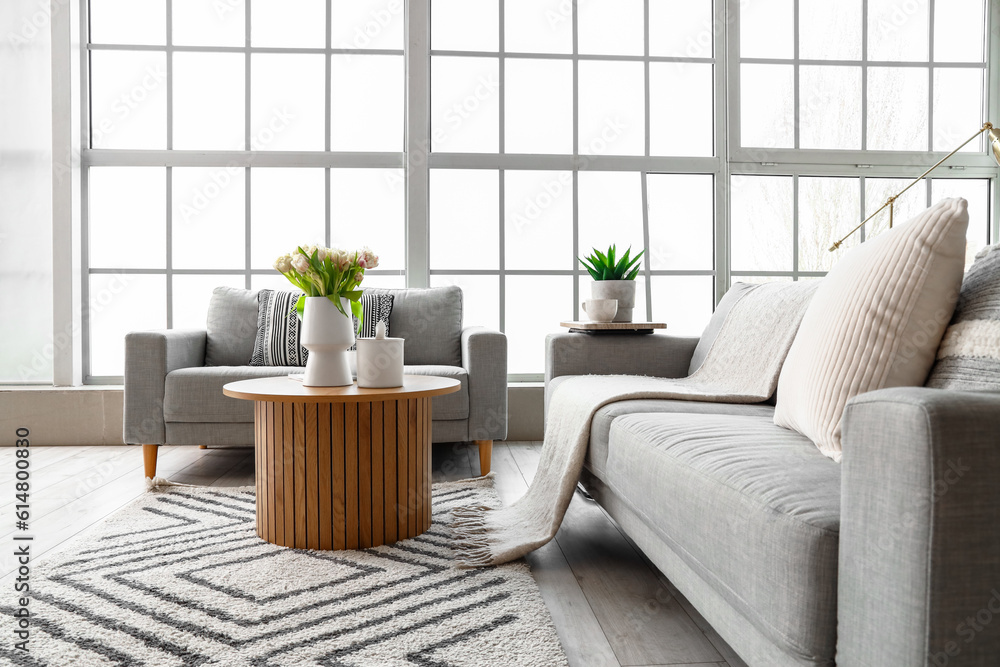 Interior of bright living room with cozy sofas and coffee table near big window