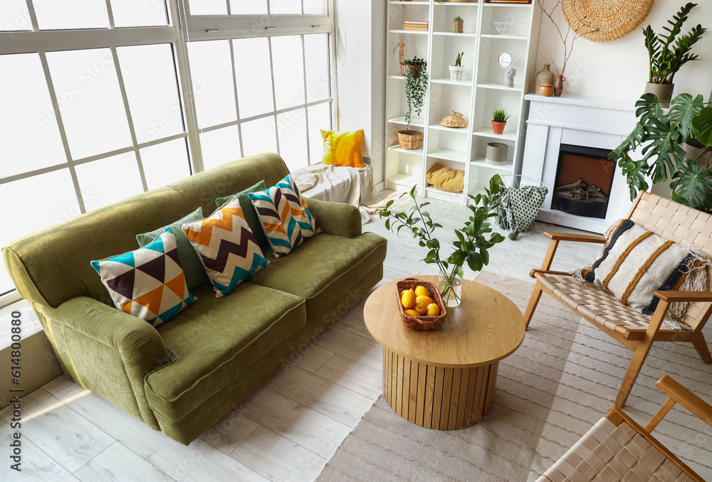 Interior of bright living room with cozy sofa, armchairs and coffee table near big window