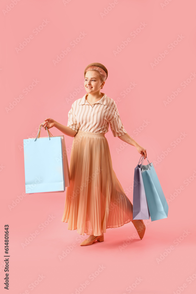 Young woman with shopping bags on pink background