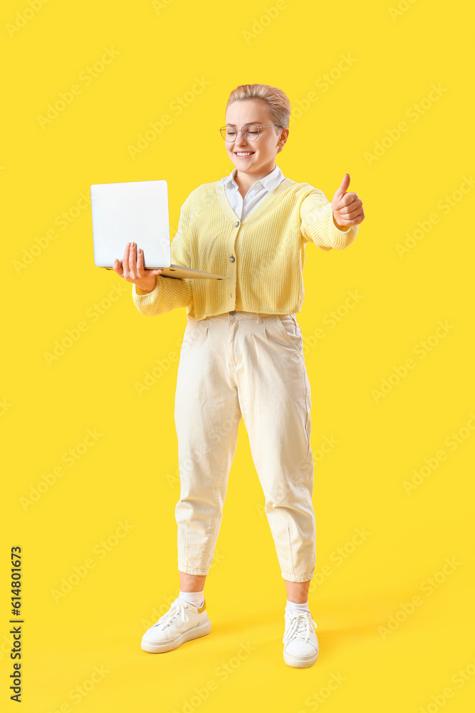 Female student with laptop showing thumb-up on yellow background