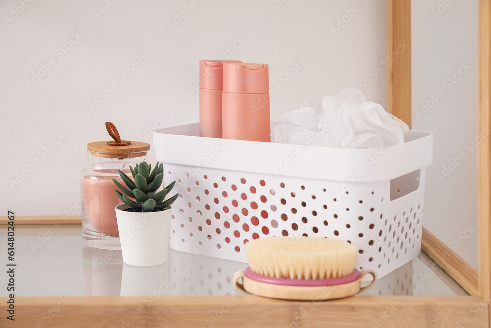 Basket with bath accessories and succulent on shelf near light wall