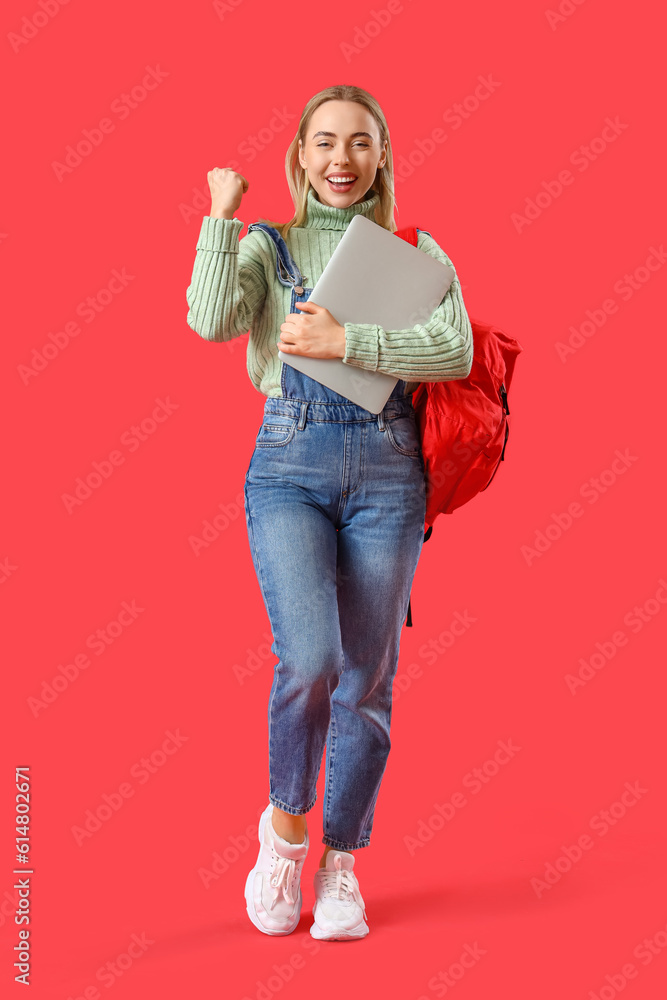 Happy female student with laptop on red background