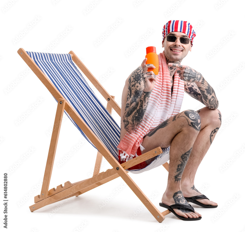 Tattooed man with sunscreen cream sitting on deck chair against white background