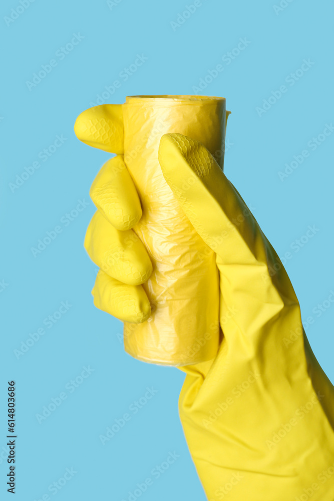 Hand in rubber glove with roll of garbage bags on blue background