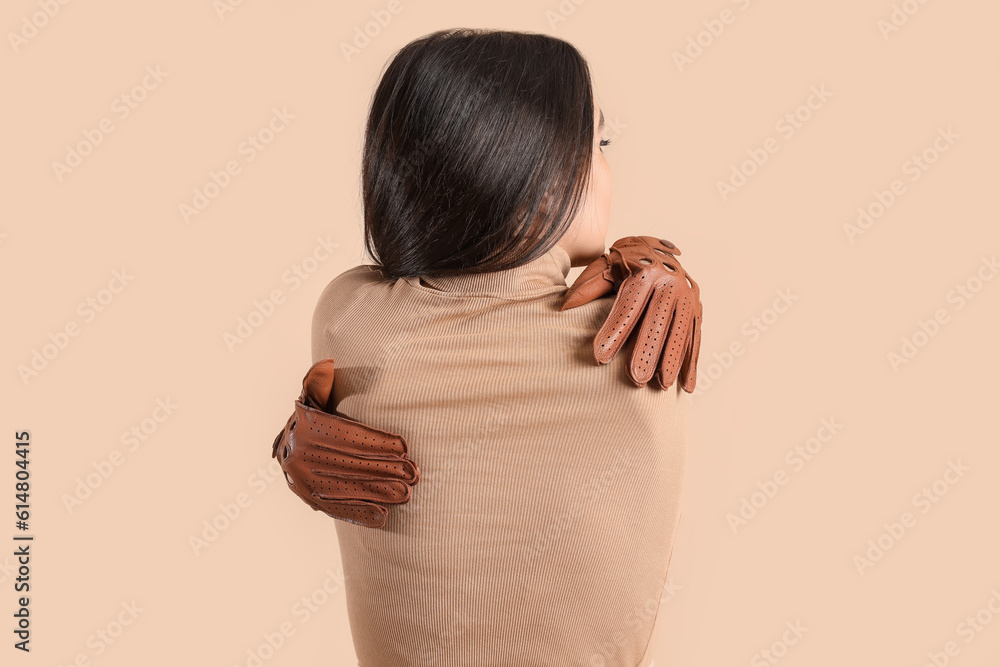 Stylish young woman in leather gloves on beige background, back view