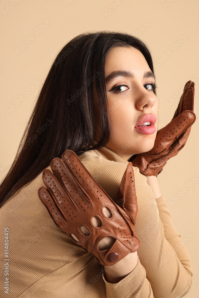 Stylish young woman in leather gloves on beige background, closeup