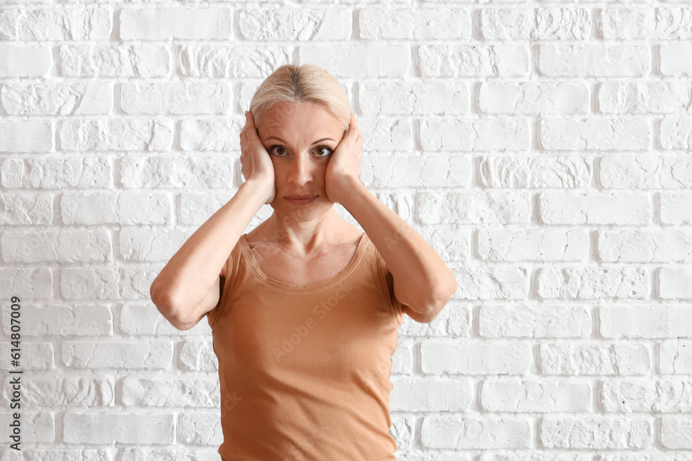 Mature woman doing face building exercise on white brick background