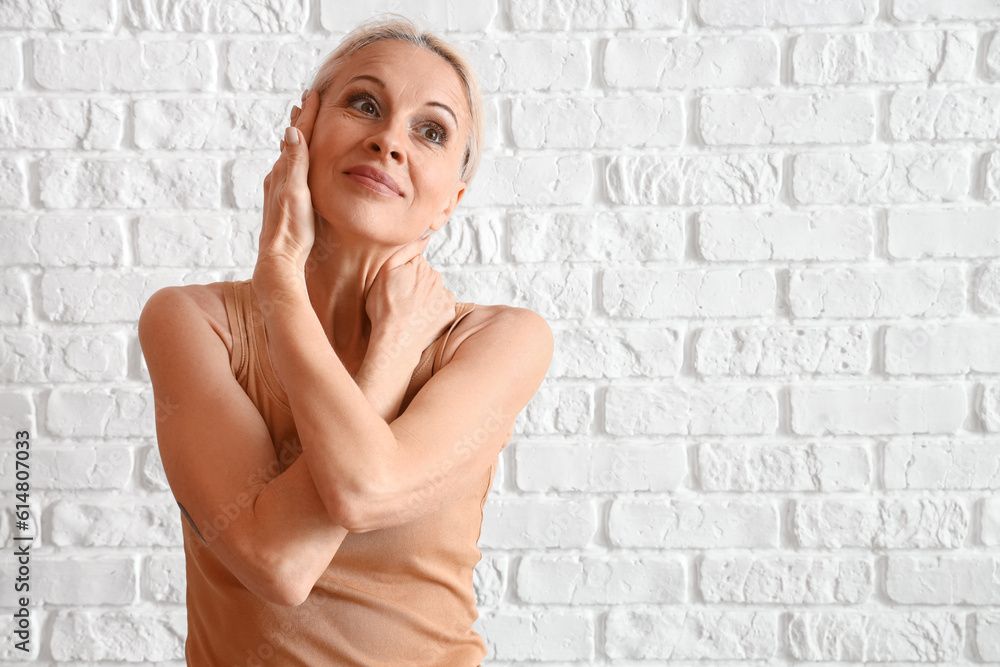 Mature woman doing face building exercise on white brick background