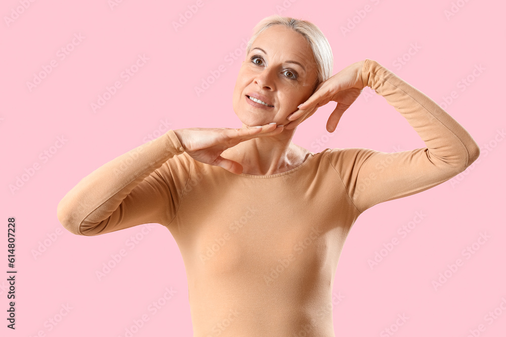 Mature woman doing face building exercise on pink background