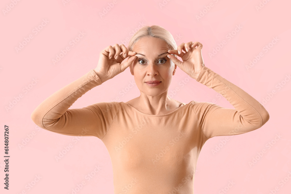 Mature woman doing face building exercise on pink background