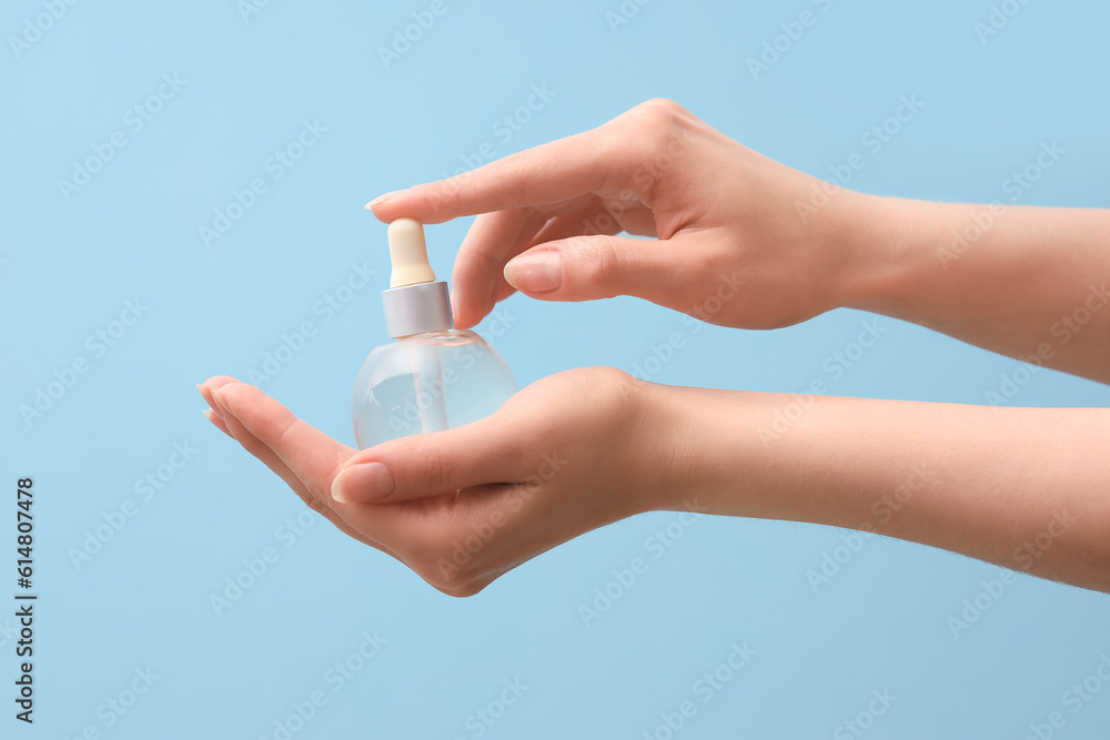 Hands holding bottle with cosmetic serum on light blue background