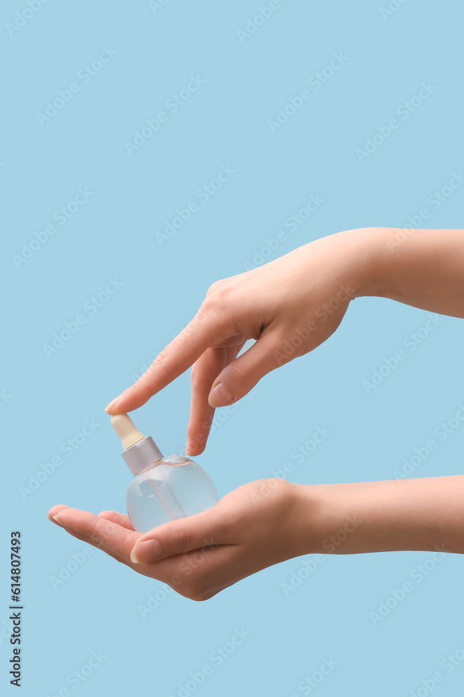 Hands holding bottle with cosmetic serum on light blue background