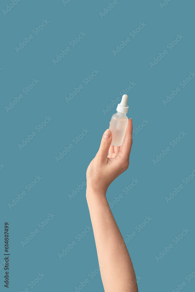 Hand holding bottle with cosmetic serum on blue background