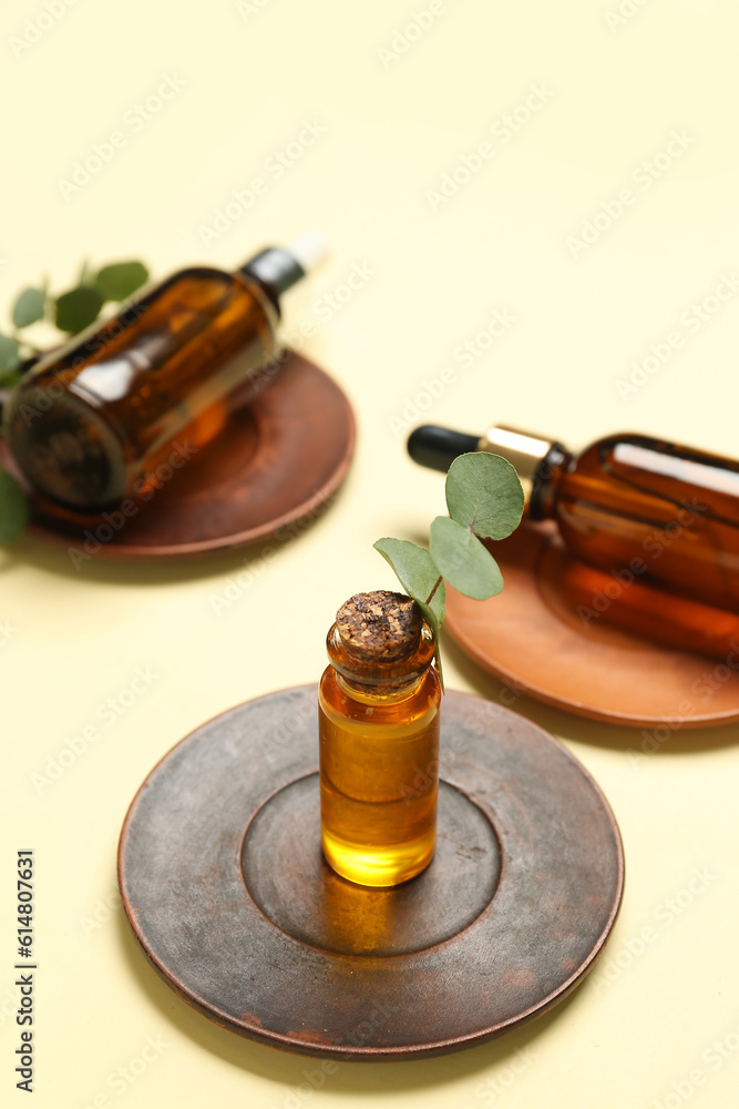 Wooden plates with bottles of cosmetic oil and eucalyptus branch on pale yellow background