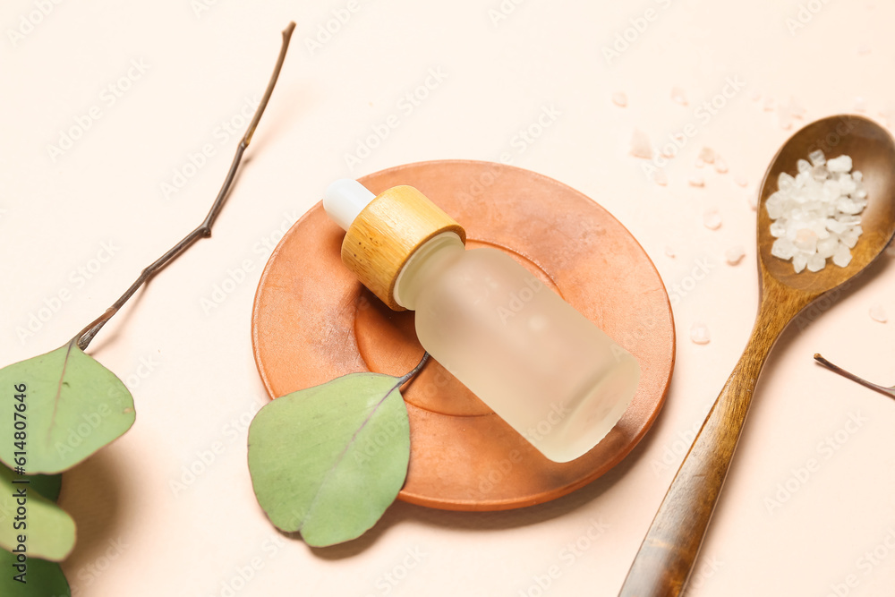 Bottle of cosmetic oil with sea salt and eucalyptus branch on beige background