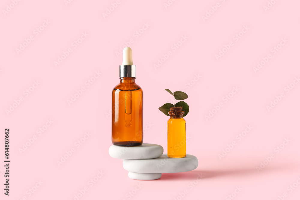 Bottles of cosmetic oil with stones on pink background