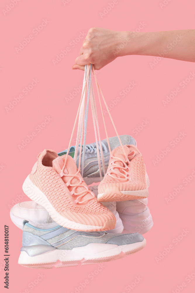 Female hand with many sneakers on pink background