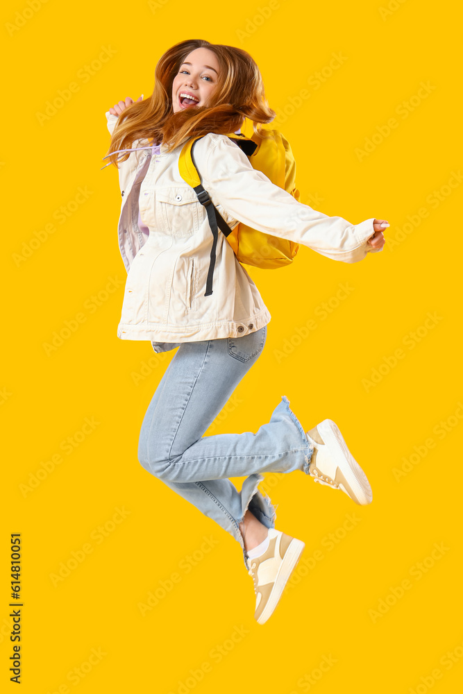 Female student jumping on yellow background