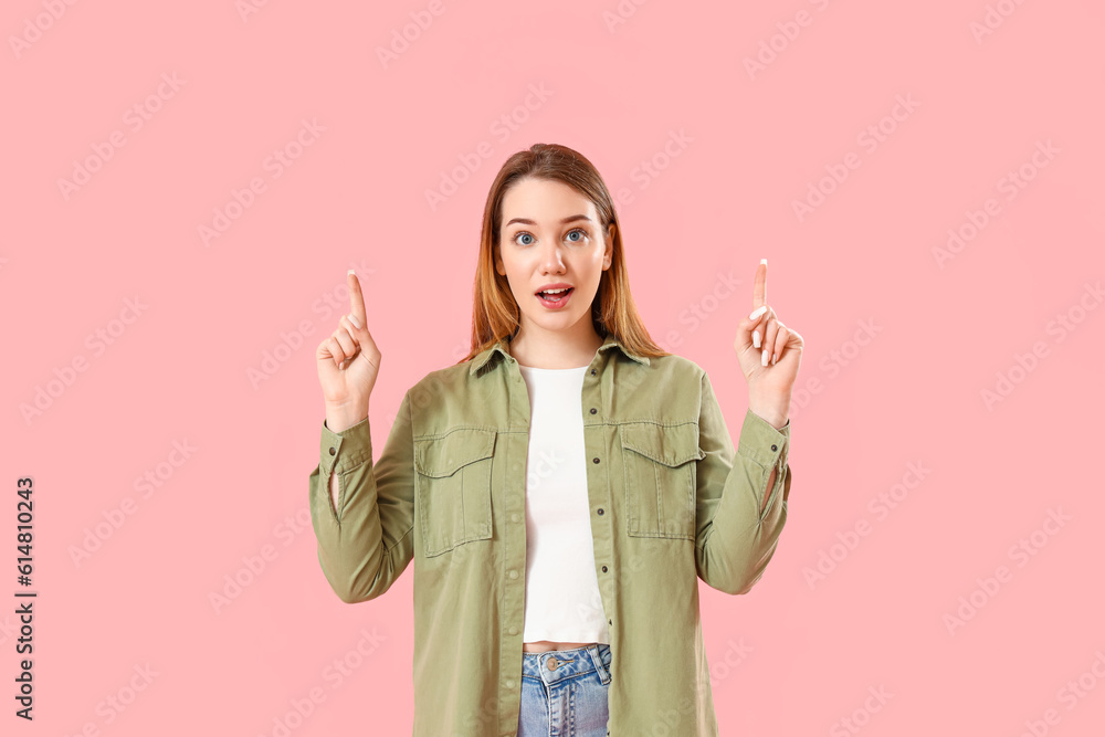 Beautiful young woman pointing at something on pink background