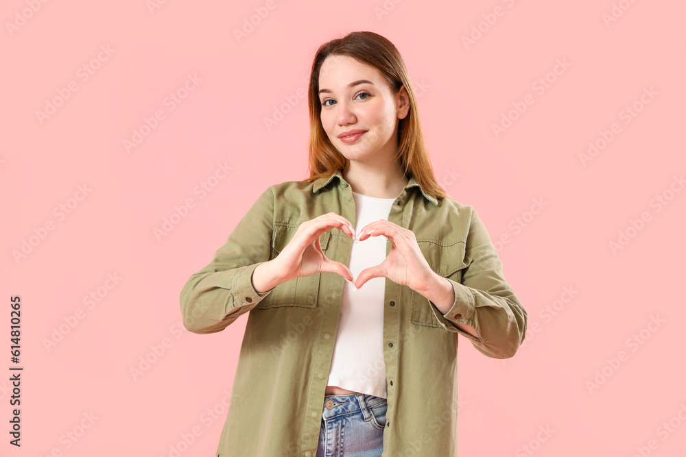 Beautiful young woman making heart with her hands on pink background