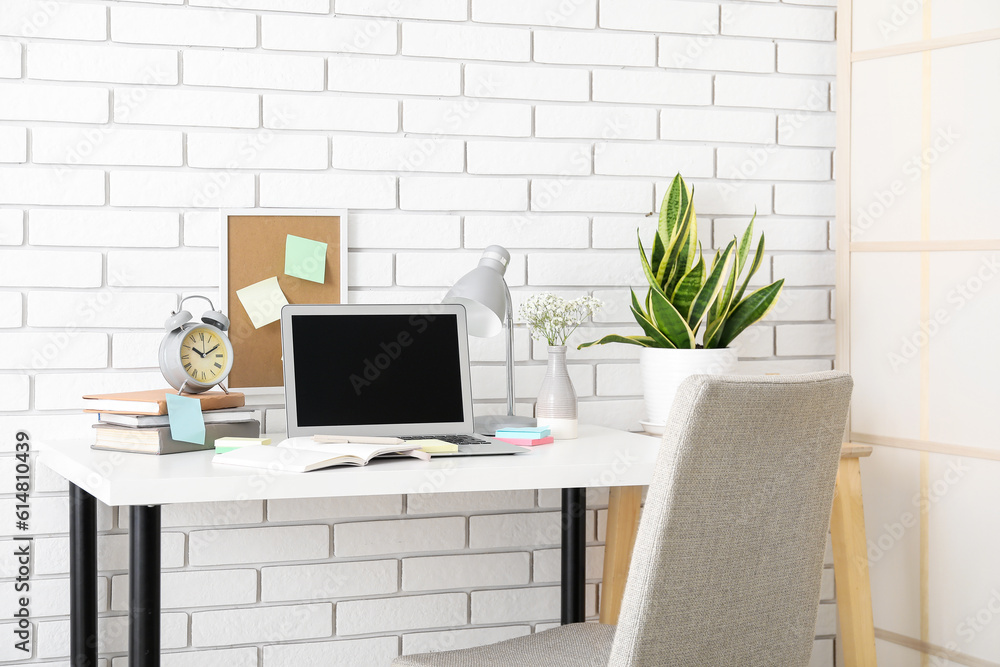 Modern workplace with laptop, sticky notes and board near brick wall