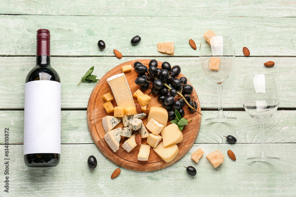 Pieces of tasty cheese, glasses and bottle with wine on green wooden background