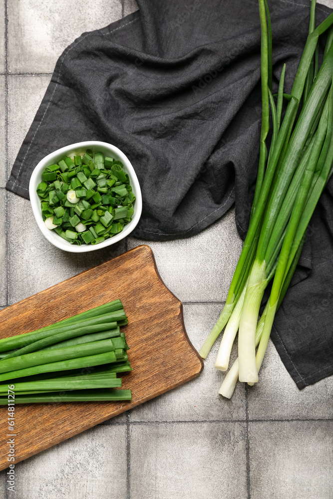 Wooden board and bowl with fresh green onion on dark tile background