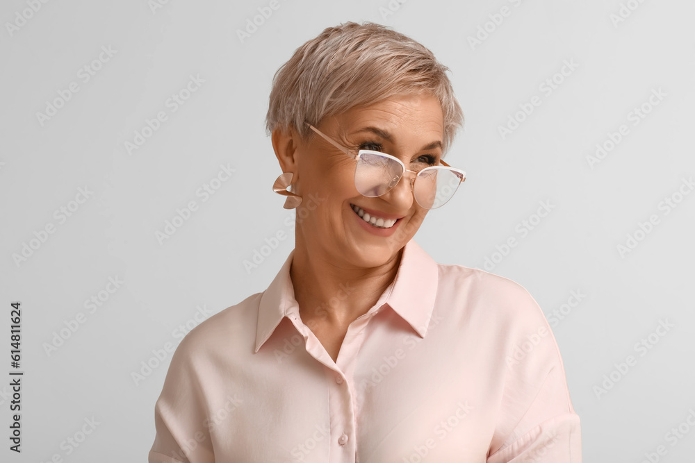 Mature blonde woman in eyeglasses on light background