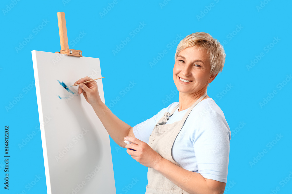 Mature female artist painting picture on blue background