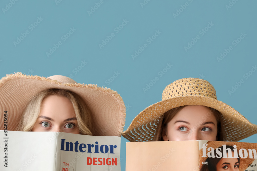 Young sisters in summer hats reading magazines on blue background, closeup