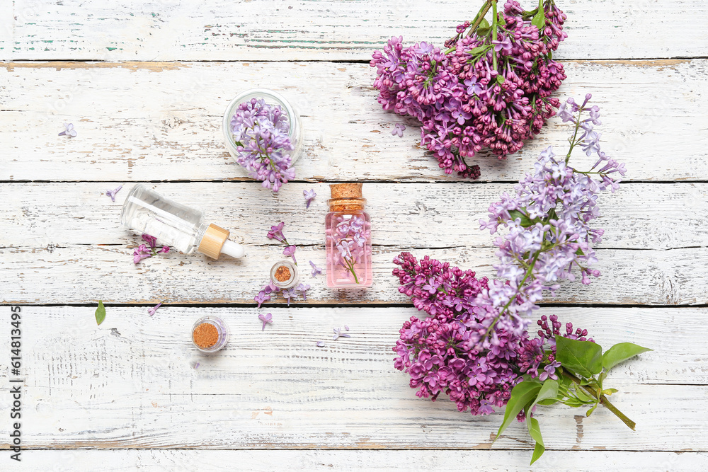 Composition with bottles of lilac essential oil and flowers on light wooden background