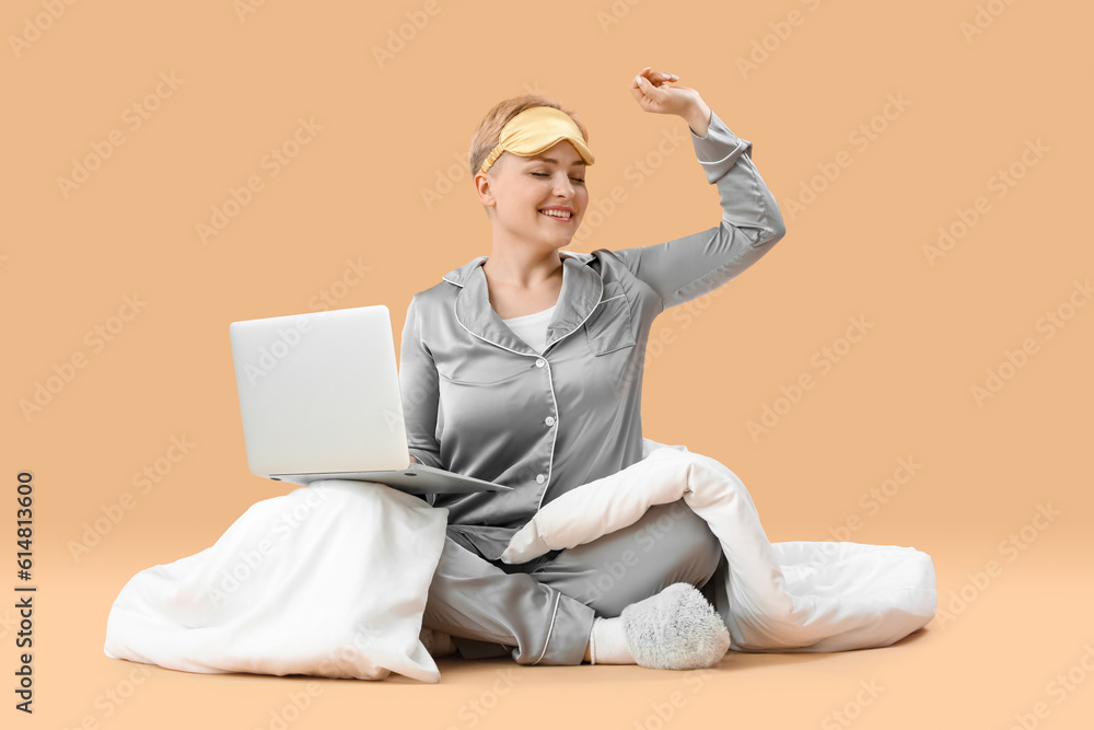 Young woman with laptop and blanket stretching on beige background