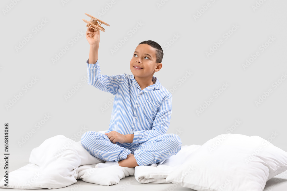 Little African-American boy with wooden plane and soft blanket on light background