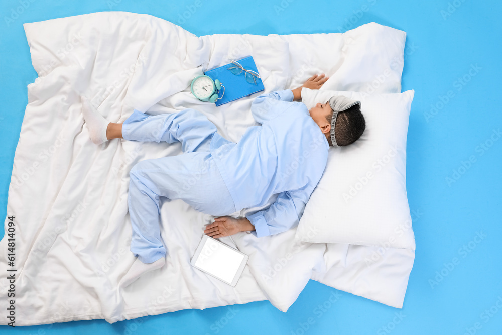 Little African-American boy with soft blanket sleeping on blue background, top view