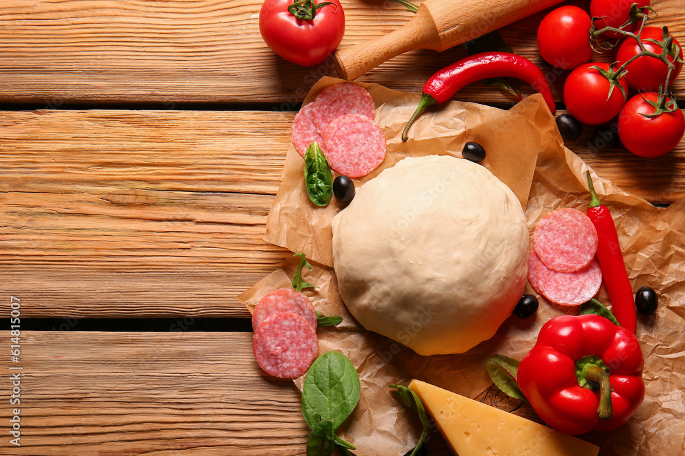 Raw dough and ingredients for preparing pizza on wooden background