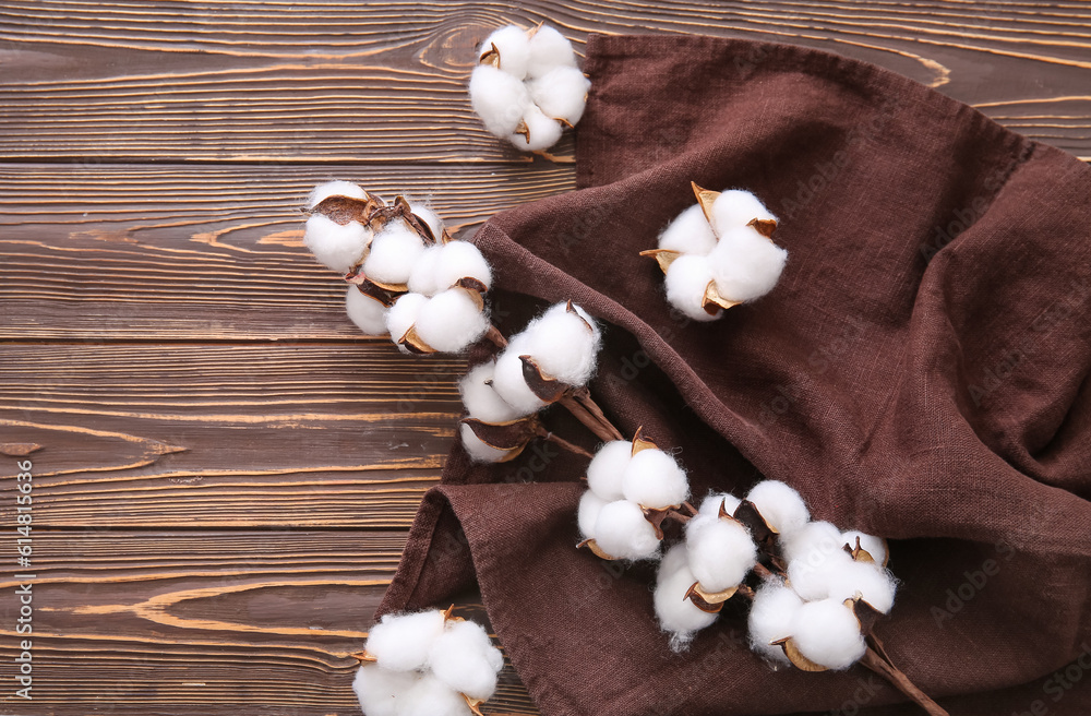 Cotton sprig with flowers and brown towel on wooden table