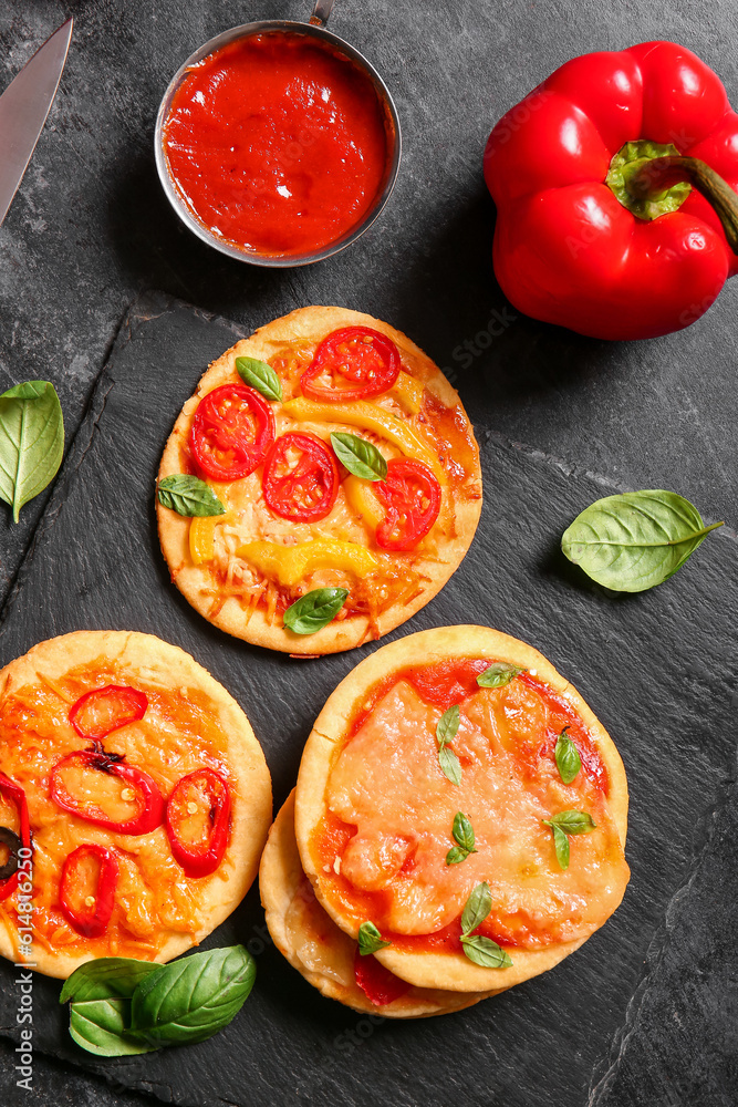 Board with different tasty mini pizzas on black background