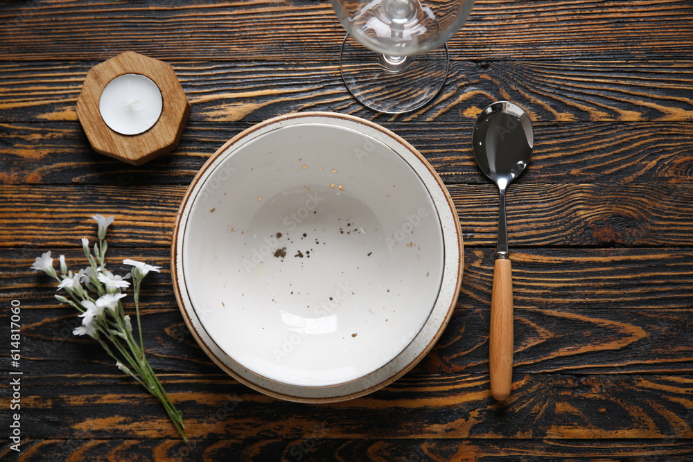 Plates with spoon, glass and candle on brown wooden background