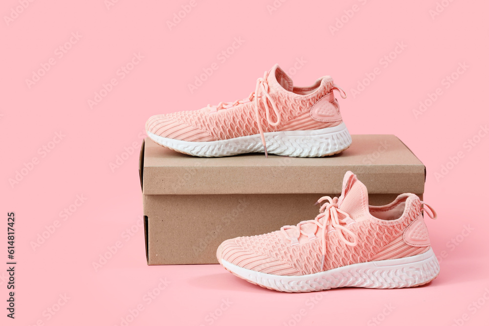 Cardboard box with stylish female sneakers on pink background