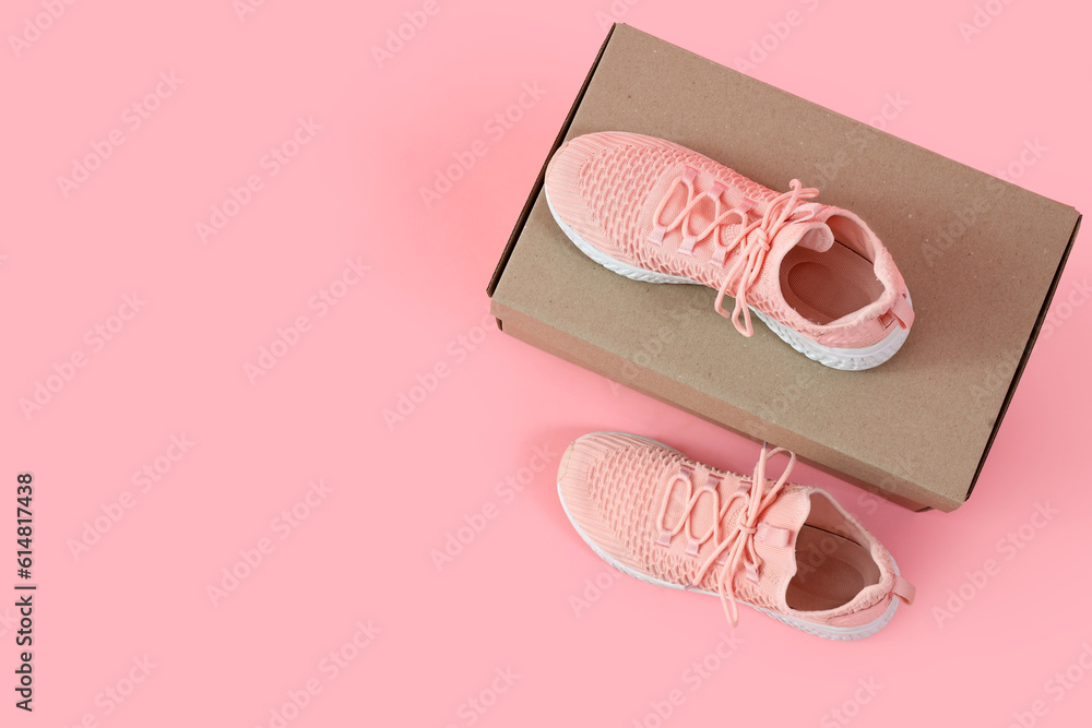 Cardboard box with stylish female sneakers on pink background