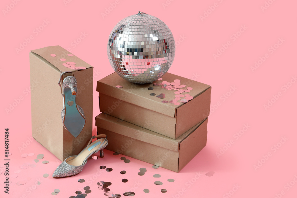 Cardboard boxes with heeled shoes, sprinkles and disco ball on pink background