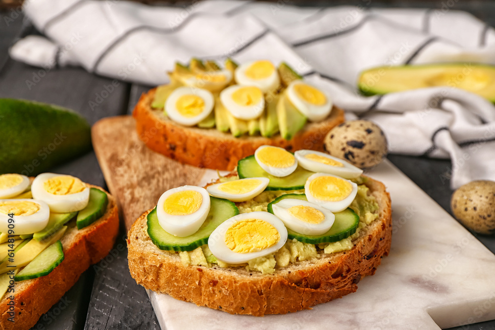 Tasty toasts with quail eggs, avocado and cucumber on dark wooden background, closeup