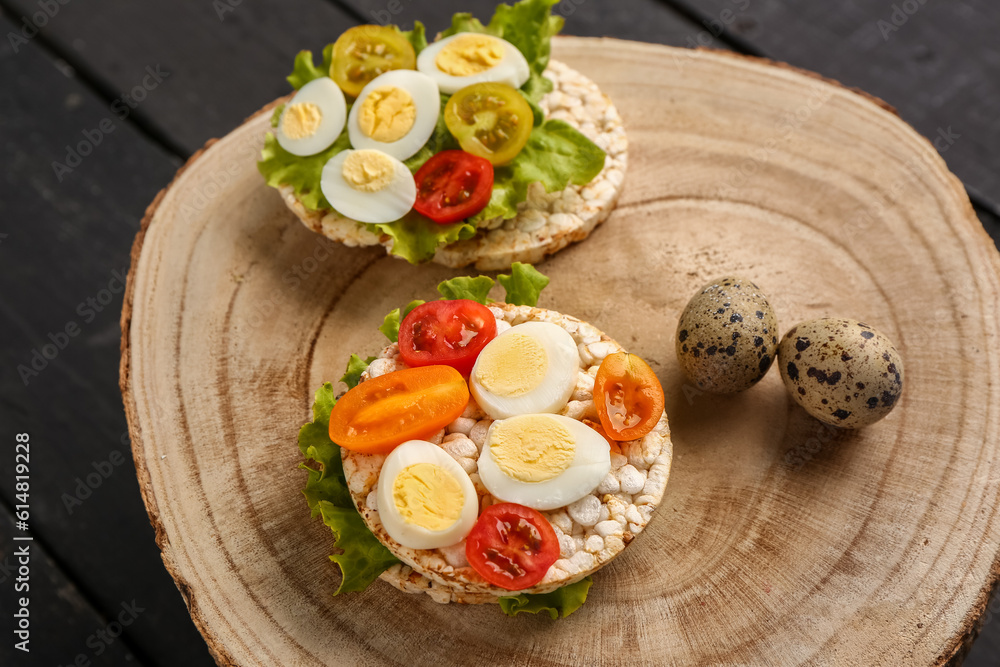 Rice crackers with quail eggs, tomatoes and lettuce on dark wooden background, closeup