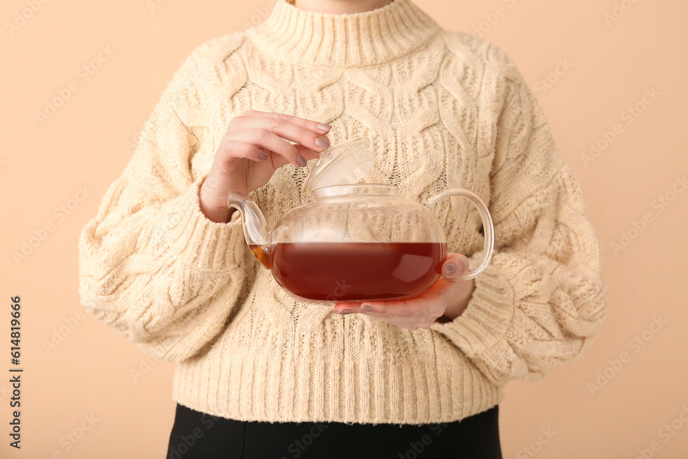 Beautiful young woman with teapot of chamomile tea near beige wall