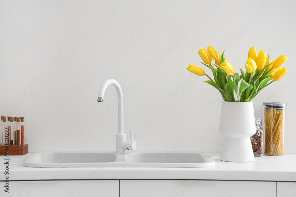 Vase with yellow tulip flowers on countertop near kitchen sink