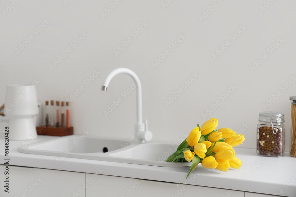 Bouquet of yellow tulip flowers on white kitchen counter near sink