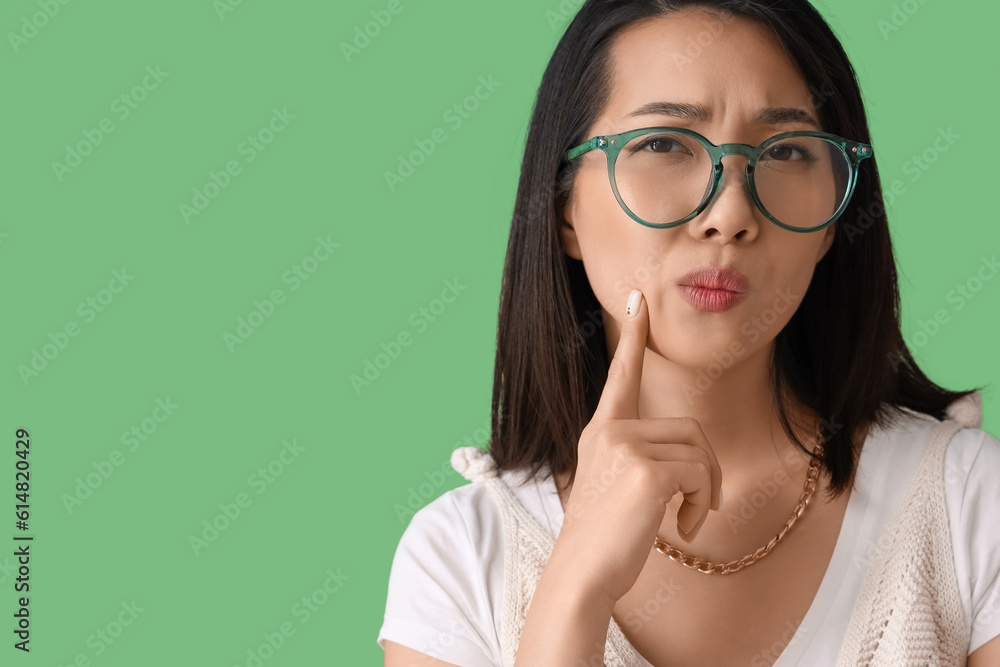 Thoughtful Asian woman in stylish eyeglasses on green background, closeup