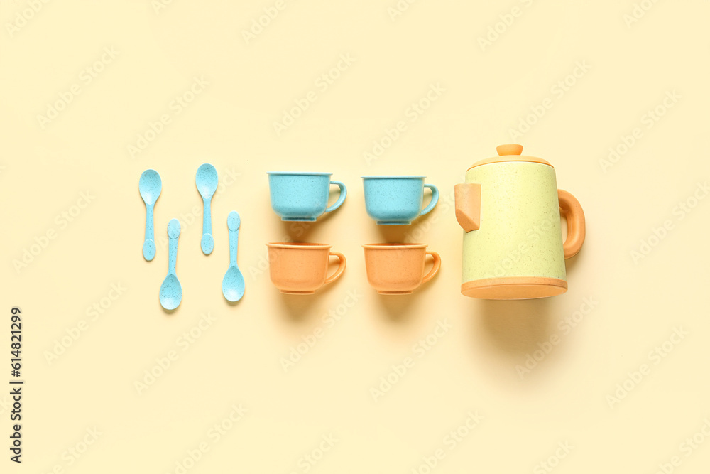 Teapot with cups and spoons on pale yellow background. Childrens Day celebration