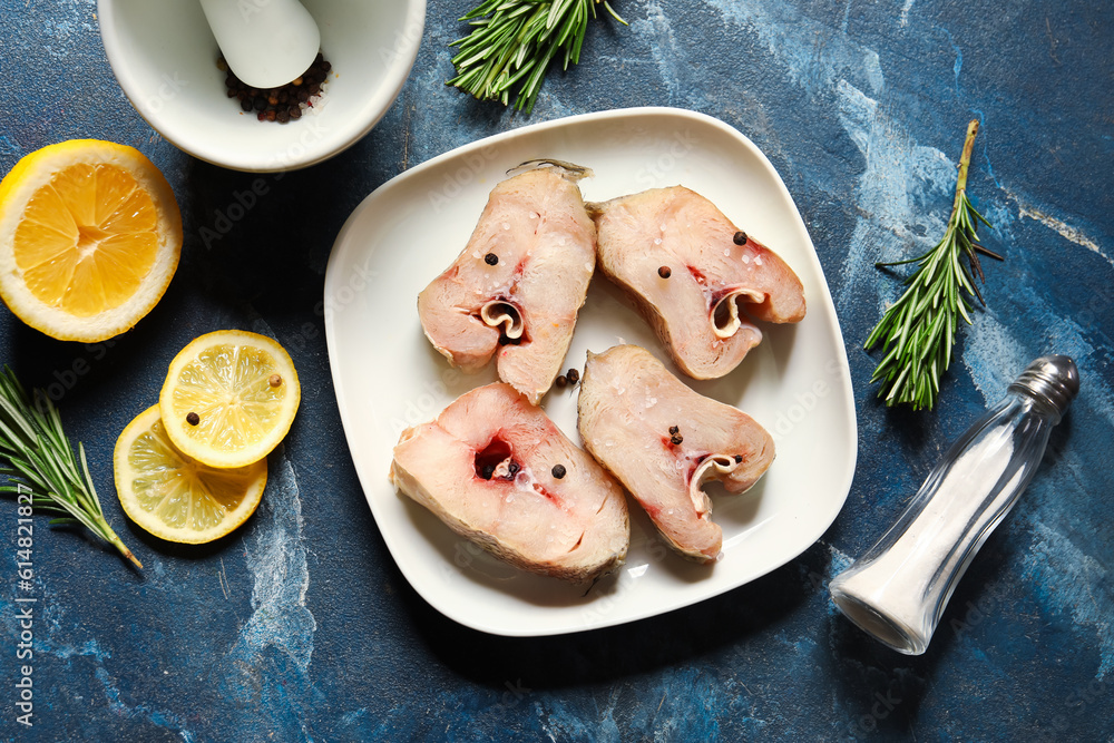 Plate with pieces of raw codfish and lemon on blue background